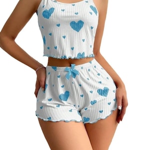 May include: White pajama set with a blue heart pattern. The set includes a camisole top and shorts, both with a ruffled trim. The shorts have a blue bow at the waist. The fabric has a ribbed texture.