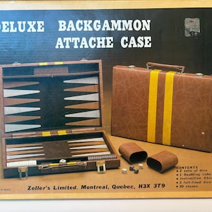 May include: A vintage Deluxe Backgammon Attache Case. The open case reveals a wooden game board with black and white triangles. A closed brown case with yellow stripes is next to it, along with dice and dice cups. The box reads "Deluxe Backgammon Attache Case."