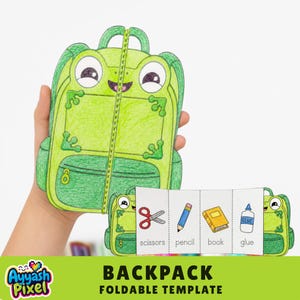 Puede incluir: Una plantilla plegable de papel en forma de mochila de rana verde con un diseño de cremallera central. El interior muestra cuatro paneles con ilustraciones de material escolar: tijeras rojas, lápiz amarillo, libro amarillo y pegamento.