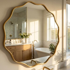Peut inclure: Un miroir doré aux bords ondulés est accroché au mur, reflétant une salle de bain. La salle de bain comprend une vanité en bois, une baignoire blanche et une fenêtre. La forme inhabituelle du miroir ajoute une touche décorative.