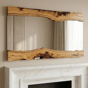 May include: A rectangular mirror with a natural wood frame. The frame has a raw, organic edge, showcasing the wood's grain and texture. The mirror is mounted above a white fireplace.