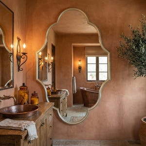 May include: A bathroom with a copper sink, a large ornate mirror, and a wooden vanity. The walls are painted in a warm terracotta color, and a small olive tree sits in a terracotta pot. The room has a rustic, elegant feel.