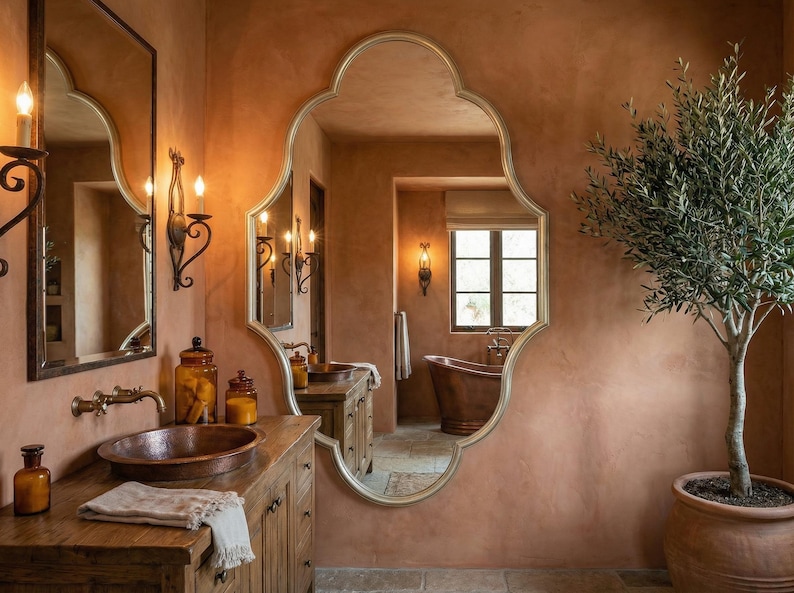 May include: A bathroom with a copper sink, a large ornate mirror, and a wooden vanity. The walls are painted in a warm terracotta color, and a small olive tree sits in a terracotta pot. The room has a rustic, elegant feel.