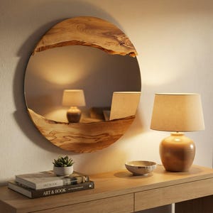 Pu&ograve; includere: Uno specchio rotondo in legno con bordo naturale &egrave; appeso al muro. Una piccola lampada e una ciotola decorativa sono su una consolle di legno. Libri e una piccola pianta in vaso sono anche sul tavolo. Lo specchio riflette una lampada.
