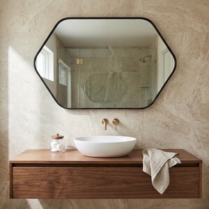 May include: A modern bathroom featuring a hexagonal black-framed mirror above a floating wooden vanity. The vanity holds a white vessel sink, gold fixtures, and a linen towel. The walls are tiled in a neutral stone pattern.
