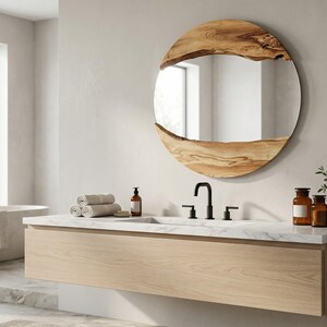 Pu&ograve; includere: Un bagno moderno con un mobile lavabo in legno chiaro e un piano in marmo. Uno specchio rotondo con una cornice in legno naturale &egrave; appeso sopra il lavandino. La stanza comprende una vasca da bagno, asciugamani e oggetti decorativi.