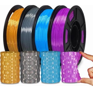 May include: Four spools of 3D printer filament in orange, grey, blue, and purple, accompanied by four matching cylindrical containers with a geometric, faceted surface texture, arranged in a row to show colour coordination.