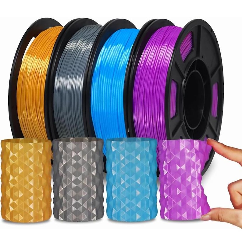 May include: Four spools of 3D printer filament in orange, grey, blue, and purple, accompanied by four matching cylindrical containers with a geometric, faceted surface texture, arranged in a row to show colour coordination.