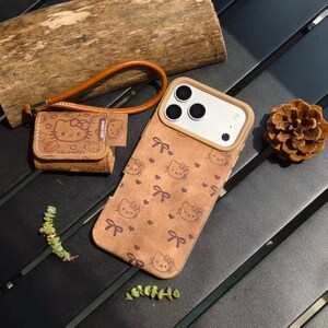 May include: Brown phone case and matching small pouch featuring a repeating Hello Kitty pattern with bows. The phone case has a camera cutout and a light brown border. The pouch has a wrist strap and the words "Hello Kitty" printed on it.