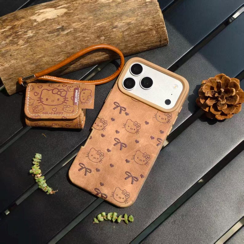May include: Brown phone case and matching small pouch featuring a repeating Hello Kitty pattern with bows. The phone case has a camera cutout and a light brown border. The pouch has a wrist strap and the words "Hello Kitty" printed on it.