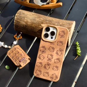 Peut inclure: Coque de t&eacute;l&eacute;phone et &eacute;tui pour accessoires de couleur beige clair, orn&eacute;s d'un motif r&eacute;p&eacute;t&eacute; de personnages Hello Kitty. La coque de t&eacute;l&eacute;phone a un bord beige clair autour des lentilles de la cam&eacute;ra. L'&eacute;tui pour accessoires porte l'inscription "Hello Kitty".