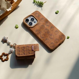 Peut inclure: Un &eacute;tui de t&eacute;l&eacute;phone marron et un petit &eacute;tui assorti, tous deux orn&eacute;s d'un motif r&eacute;p&eacute;t&eacute; de personnages Hello Kitty. L'&eacute;tui du t&eacute;l&eacute;phone a une d&eacute;coupe pour l'appareil photo. Un charm avec des &eacute;toiles et des perles est attach&eacute; au petit &eacute;tui.