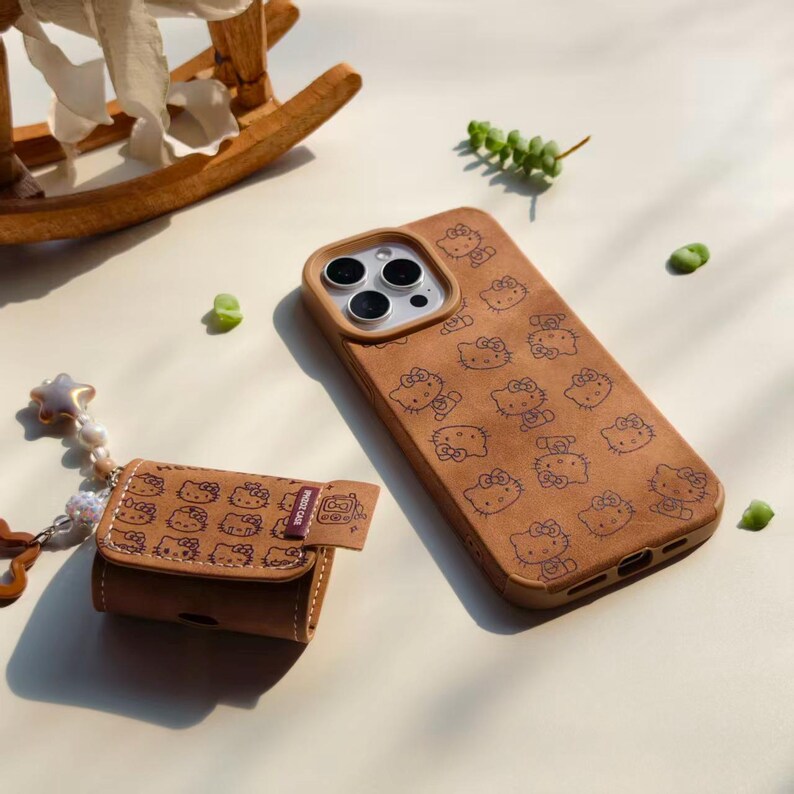 Peut inclure: Coque de t&eacute;l&eacute;phone marron et &eacute;tui pour &eacute;couteurs assorti, avec un motif r&eacute;p&eacute;t&eacute; d'un chat de dessin anim&eacute;. L'&eacute;tui du t&eacute;l&eacute;phone a une d&eacute;coupe pour l'appareil photo et un bord marron. L'&eacute;tui des &eacute;couteurs porte le texte "PHONE CASE".