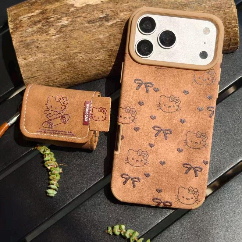 K&ouml;nnte beinhalten: Braune Handyh&uuml;lle und passendes AirPod-Case mit einem sich wiederholenden Muster aus Hello Kitty-Gesichtern und Schleifen. Die Handyh&uuml;lle hat einen beigen Rand. Das AirPod-Case hat eine Hello Kitty-Grafik.