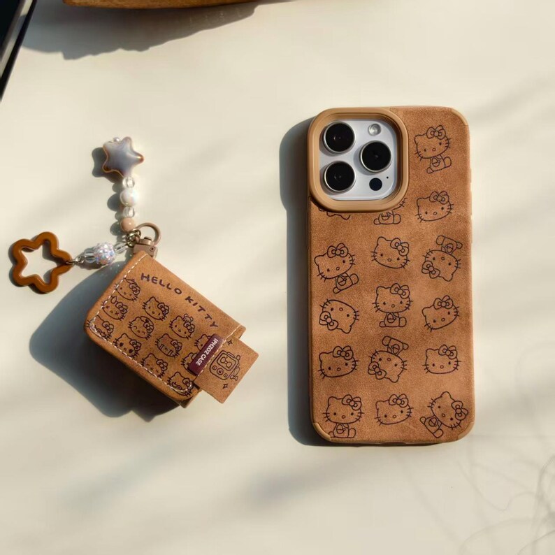 Peut inclure: Un &eacute;tui de t&eacute;l&eacute;phone marron et un accessoire assorti avec un motif Hello Kitty r&eacute;p&eacute;t&eacute;. L'&eacute;tui de t&eacute;l&eacute;phone a une d&eacute;coupe pour l'appareil photo et un charm en forme d'&eacute;toile. L'accessoire porte l'inscription "Hello Kitty".