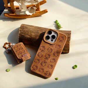 Peut inclure: Coque de t&eacute;l&eacute;phone marron et petite pochette assortie avec un motif Hello Kitty r&eacute;p&eacute;t&eacute;. L'&eacute;tui du t&eacute;l&eacute;phone a une d&eacute;coupe pour l'appareil photo et un bord marron clair. La pochette a un charm en forme d'&eacute;toile et l'inscription "Hello Kitty".