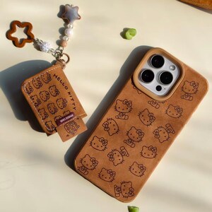 Peut inclure: Un &eacute;tui de t&eacute;l&eacute;phone marron et un accessoire assorti avec un motif Hello Kitty r&eacute;p&eacute;t&eacute;. L'&eacute;tui a une d&eacute;coupe pour l'appareil photo et un bord marron. L'accessoire porte le texte "HELLO KITTY" et un charm en forme d'&eacute;toile.