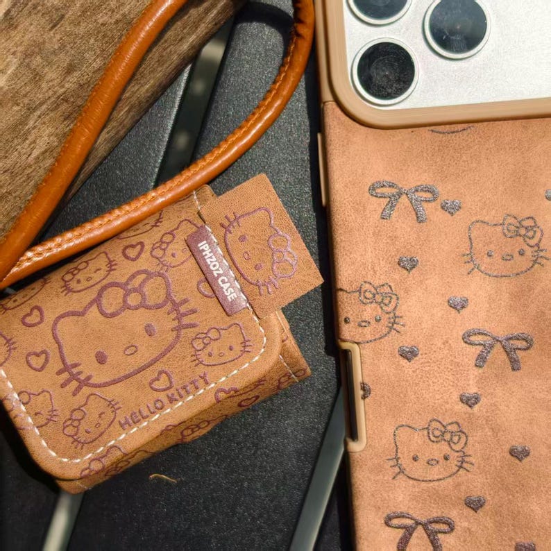 May include: Brown phone case and matching small pouch featuring Hello Kitty designs. The case has a strap and a matching pouch with the text "IPHZOZ CASE" and "HELLO KITTY". The case has a bow and heart pattern.