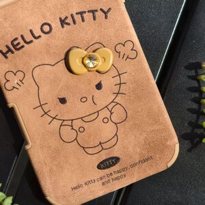 May include: A brown Hello Kitty phone case with a bow and a gem. The case features a Hello Kitty illustration and the text "HELLO KITTY". The case also has the text "Hello kitty can be happy, confident and happy".