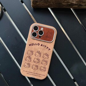 Op de afbeelding: Tan telefoonhoesje met het Hello Kitty-logo en meerdere illustraties van het personage. De hoes heeft een bruin lederlook accent rond de cameralenzen en de tekst "HELLO KITTY" staat op de hoes.