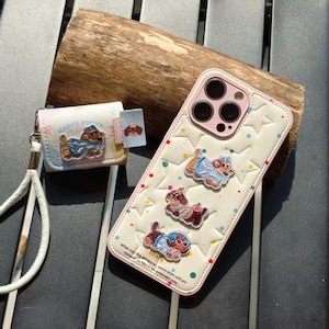 May include: A cream-colored phone case and small pouch featuring embroidered dog designs. The phone case has a pink border and star pattern. The pouch has a wrist strap. The text on the phone case reads "When you like someone, your brain will put makeup on him in an automatic way."