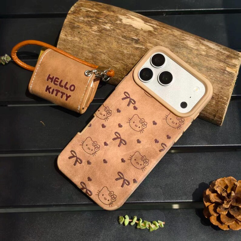 K&ouml;nnte beinhalten: Eine braune Handyh&uuml;lle mit Hello Kitty-Muster und einem passenden kleinen T&auml;schchen. Die Handyh&uuml;lle hat einen beigefarbenen Rand um die Kameralinsen. Auf dem T&auml;schchen steht "HELLO KITTY".