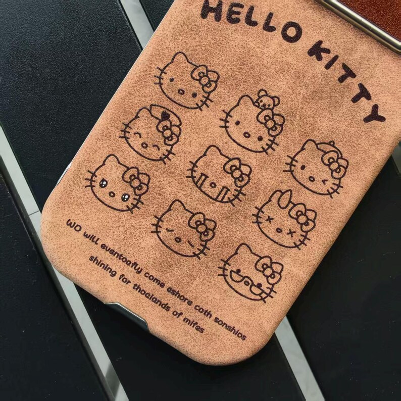Op de afbeelding: Bruine telefoonhoes met meerdere Hello Kitty-illustraties. De woorden "HELLO KITTY" staan bovenaan en een citaat onderaan. De hoes is gemaakt van een textuurrijk materiaal.