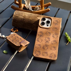 May include: Brown phone case and matching small case featuring a repeating pattern of Hello Kitty characters. The phone case has a tan border around the camera lenses. The small case has a snap closure and a small logo.