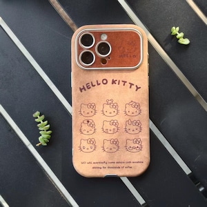 Op de afbeelding: Een bruine telefoonhoes met een Hello Kitty-ontwerp. De hoes heeft een bruine cameralensbeschermer en de woorden "HELLO KITTY" staan bovenaan gedrukt. De hoes heeft meerdere Hello Kitty-karakterillustraties.