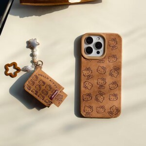 Peut inclure: Coque de t&eacute;l&eacute;phone marron et porte-cartes assorti, avec un motif Hello Kitty r&eacute;p&eacute;t&eacute;. L'&eacute;tui de t&eacute;l&eacute;phone a une d&eacute;coupe pour l'appareil photo et un bord marron clair. Le porte-cartes a un charm en forme d'&eacute;toile et l'inscription "Hello Kitty".