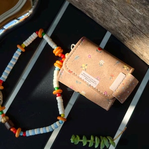 May include: A small, tan wallet with a floral pattern and a small tag that reads "Next time you see me bring a bunch of flowers." A colorful beaded necklace and a small succulent are also in the image.