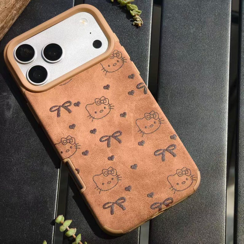 May include: A brown phone case featuring a repeating pattern of Hello Kitty faces, bows, and hearts. The case has a tan border around the camera and phone edges. The case is designed to fit a smartphone.