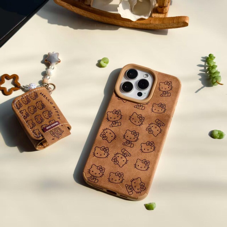 Peut inclure: Un &eacute;tui de t&eacute;l&eacute;phone marron et un &eacute;tui accessoire assorti, tous deux orn&eacute;s d'un motif Hello Kitty noir r&eacute;p&eacute;t&eacute;. L'&eacute;tui du t&eacute;l&eacute;phone a une d&eacute;coupe pour l'appareil photo et un bord de couleur claire. Un charm en forme d'&eacute;toile et une &eacute;toile en bois sont attach&eacute;s &agrave; l'&eacute;tui accessoire.