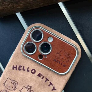 Op de afbeelding: Een tan telefoonhoesje met een bruine cameralens cover. De hoes heeft de woorden "HELLO KITTY" en een Hello Kitty-afbeelding. De cameralens cover heeft het woord "HELLO" en een Hello Kitty-afbeelding.