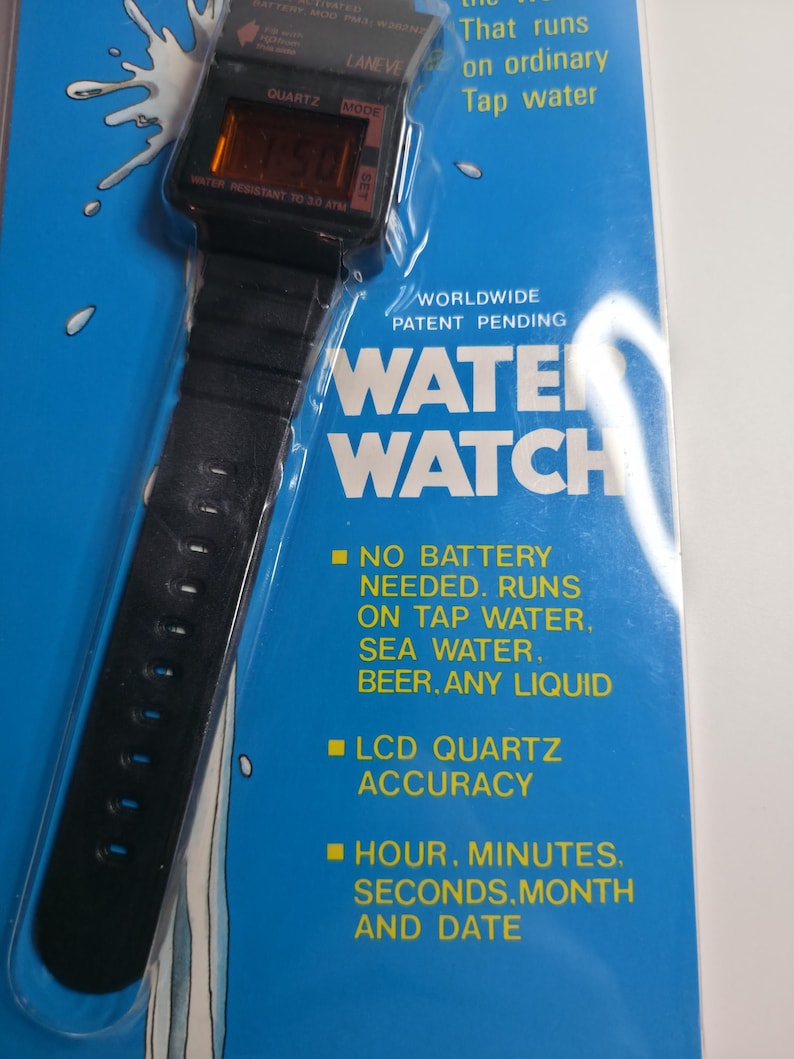 May include: A black digital Water Watch with a black band, displayed on a blue background. The watch face shows the time. Text on the packaging reads "Water Watch" and "No battery needed. Runs on tap water, sea water, beer, any liquid."