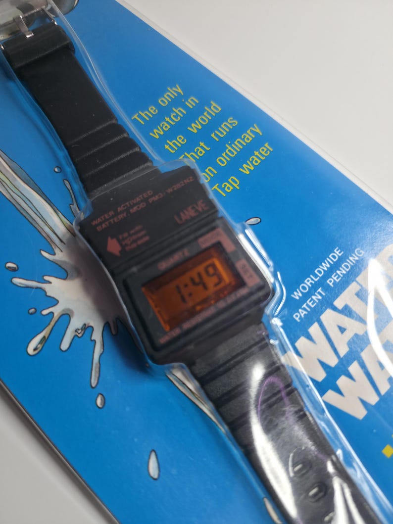 May include: A black digital watch with a black strap, displaying the time 1:49. The watch is packaged on a blue background with text that reads "The only watch in the world that runs on ordinary tap water."