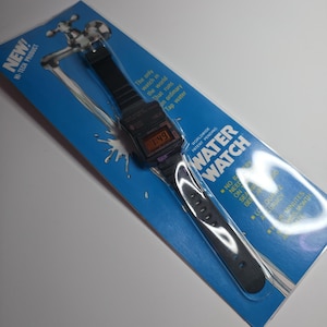 May include: A black digital Water Watch on a blue and white package. The watch displays the time 1:49. The package has the text "NEW! HI-TECH PRODUCT" and "WATER WATCH". The watch is described as running on tap water.