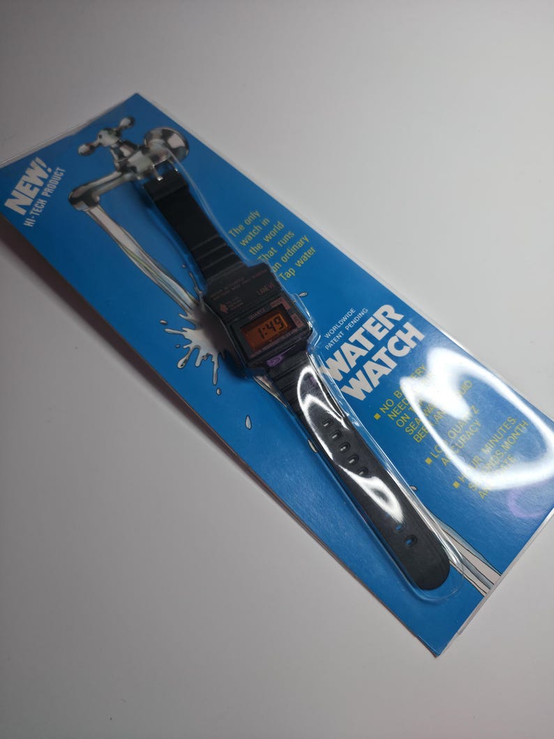 May include: A black digital Water Watch on a blue and white package. The watch displays the time 1:49. The package has the text "NEW! HI-TECH PRODUCT" and "WATER WATCH". The watch is described as running on tap water.