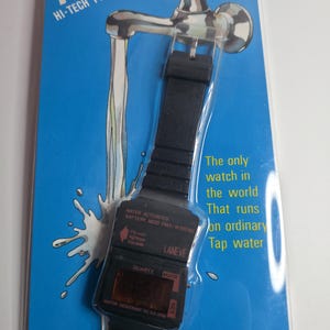 May include: A black digital watch with a black band, packaged on a blue card with a faucet illustration. The watch has the text "WATER ACTIVATED" and "WATER RESISTANT TO 20 ATM". The card reads "NEW! HI-TECH PRODUCT".