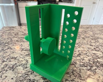 May include: A bright green 3D-printed tool holder with a screw mechanism and multiple holes. The holder has a rectangular base and a vertical support structure with a series of evenly spaced circular holes. The design suggests a tool organization system.