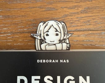 May include: A white and black illustration of a cartoon character with pointed ears and pigtails. The illustration is on top of a book with the text "DESIGN THINGS" and the name "DEBORAH NAS". The background is a wooden surface.