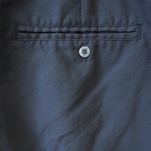 May include: Close-up of navy blue fabric with a pocket and button detail. The pocket is rectangular and stitched into the fabric. A small, round button is centered below the pocket.