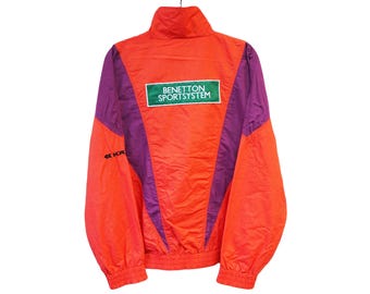 Può includere: Giacca vintage arancione e viola Benetton SportSystem. La giacca presenta un collo alto, un logo verde e bianco sul retro e polsini ed orlo elasticizzati. La giacca è realizzata in materiale leggero.