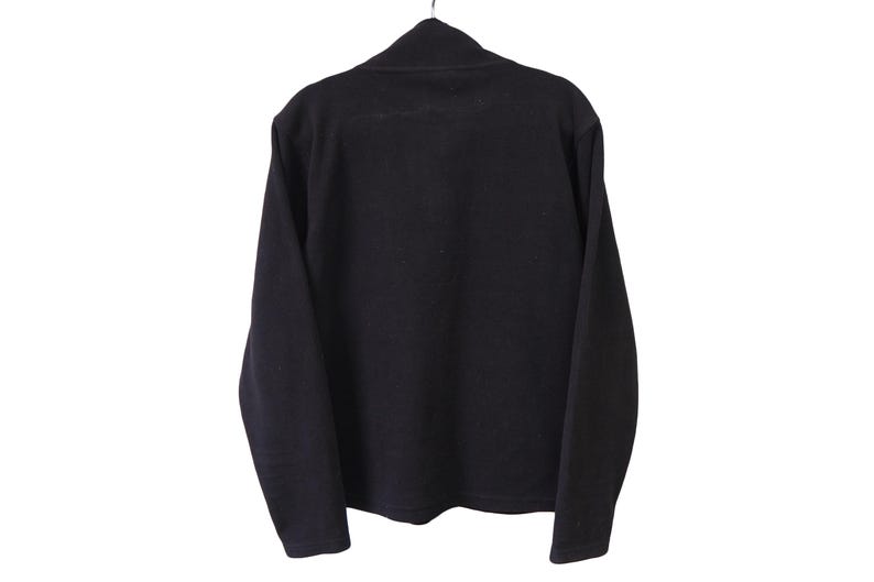 May include: A black long-sleeved shirt with a mock neck collar. The shirt is hanging on a metal hanger against a white background. The fabric appears to be a soft knit material.