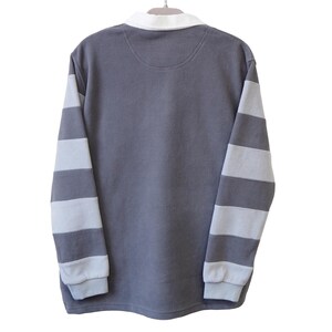 May include: A gray long-sleeved shirt with white and gray striped sleeves, a white collar, and a small patch on the back. The shirt is hanging on a white hanger against a white background.