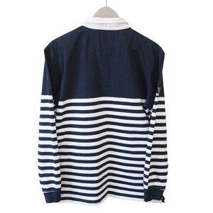 May include: Navy blue and white striped long-sleeve shirt with a white collar. The shirt is hanging on a hanger against a white background. The sleeves have horizontal stripes.