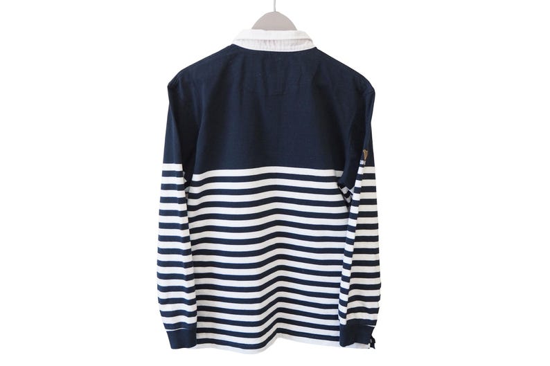 May include: Navy blue and white striped long-sleeve shirt with a white collar. The shirt is hanging on a hanger against a white background. The sleeves have horizontal stripes.