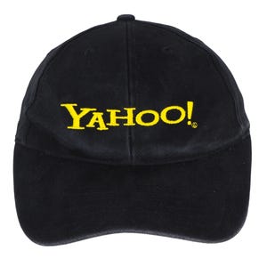 May include: A black baseball cap featuring the word YAHOO! embroidered in bright yellow thread across the front centre. The cap has a structured six-panel crown, a curved brim, and a small registered trademark symbol next to the exclamation point.