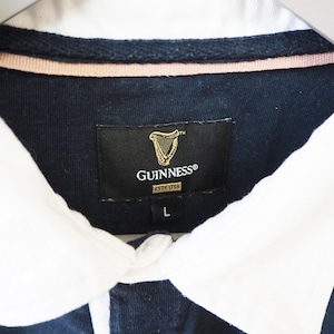 May include: Close-up of a navy blue rugby shirt with a white collar. The shirt features a Guinness label with a gold harp logo and the text "GUINNESS ESTD 1759". The size "L" is visible.