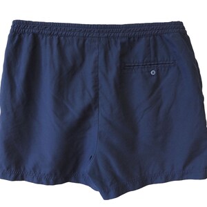 May include: Navy blue shorts with an elastic waistband and a single back pocket. The shorts are made of a lightweight fabric, ideal for warm weather. The back pocket has a button closure. The shorts are shown against a white background.